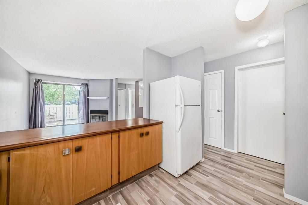 Bright kitchen with wood cabinets, white refrigerator, and striped flooring beside a windowed counter