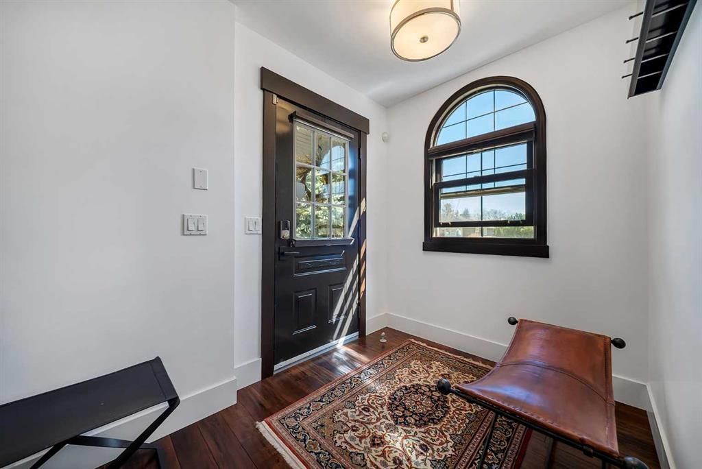Bright entryway with black front door, arched window, patterned rug, and brown chair on white walls.