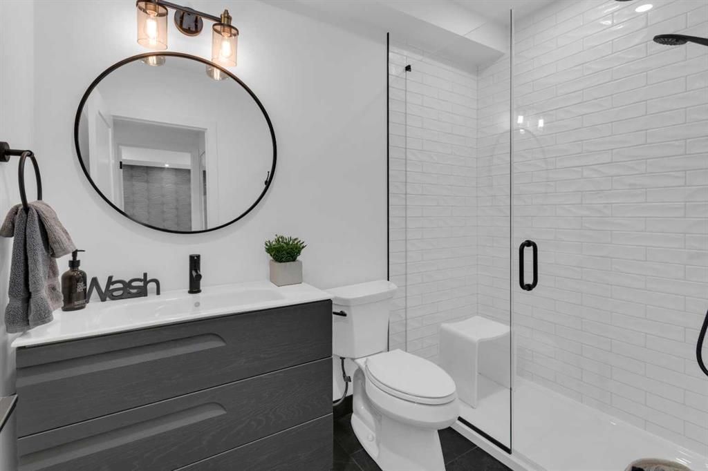 Modern bathroom with dark vanity, round mirror, toilet, and glass shower enclosure