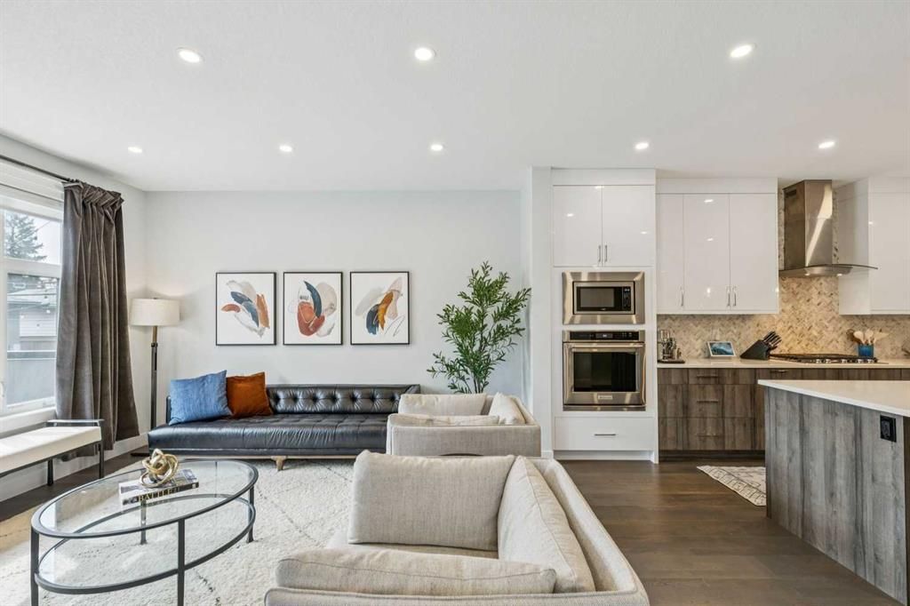 Bright modern living room with gray sofa, glass coffee table, kitchen island, and built-in oven.