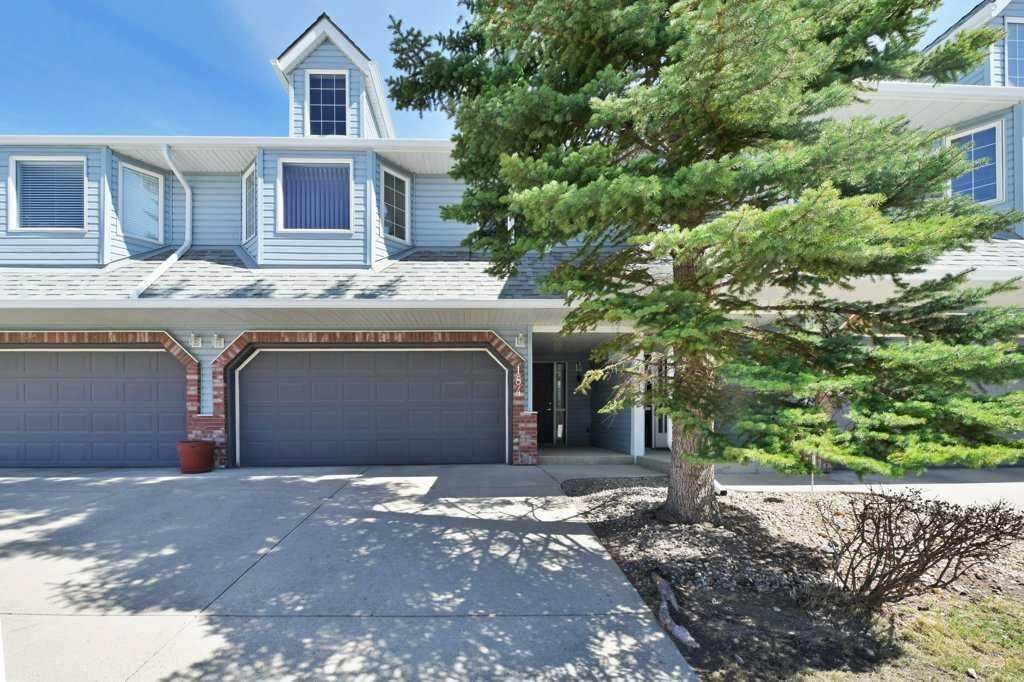 Two-story suburban house with two-car garage, gray siding, and large evergreen tree in front yard
