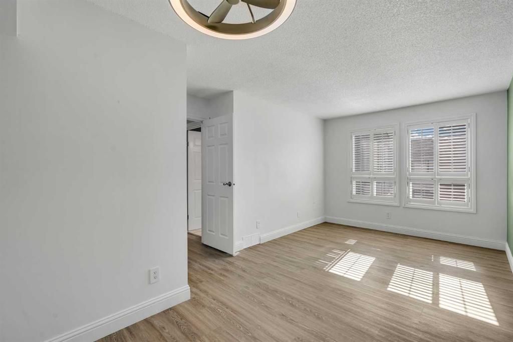 Bright empty room with white walls, light wood floors, and sunlight through large windows.