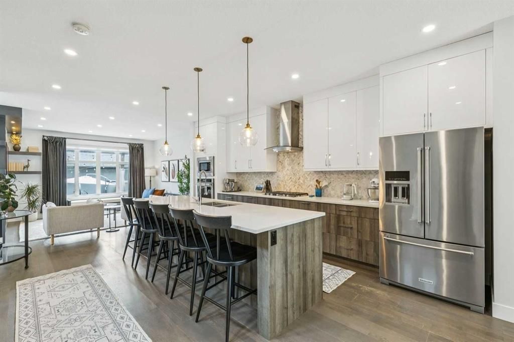 Bright modern kitchen with white cabinets, marble island, black stools, and stainless steel refrigerator.