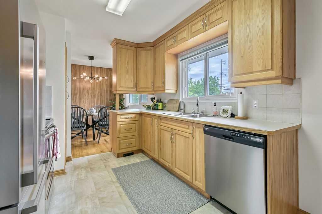 Bright kitchen with wooden cabinets, stainless steel appliances, tiled floor, and a window over the sink.