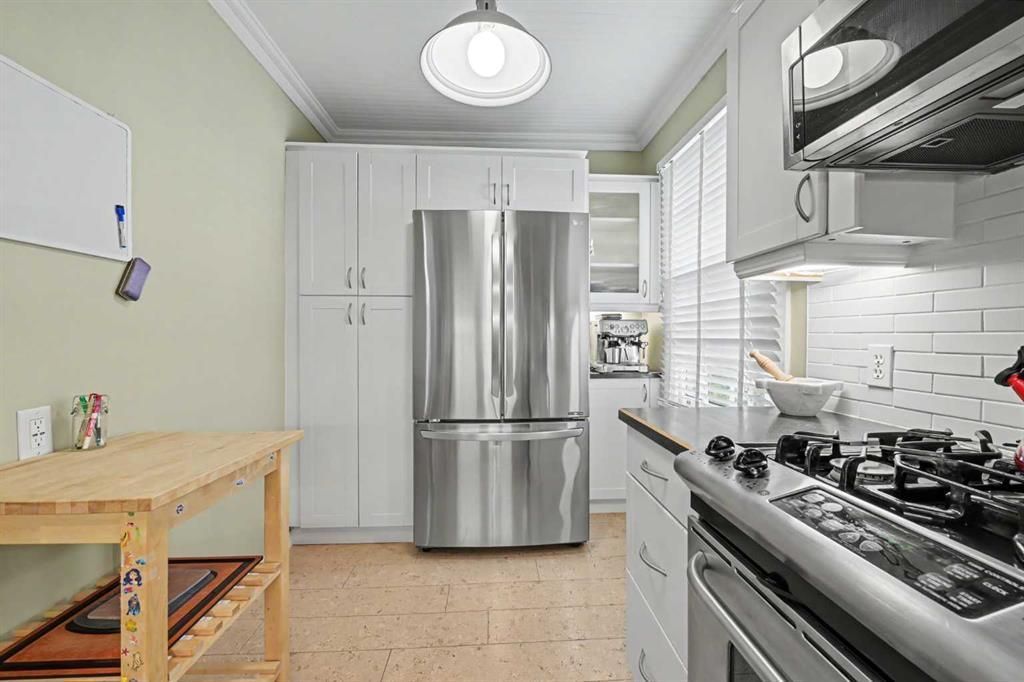 Bright modern kitchen with stainless steel refrigerator, gas stove, white cabinets, and wooden island table