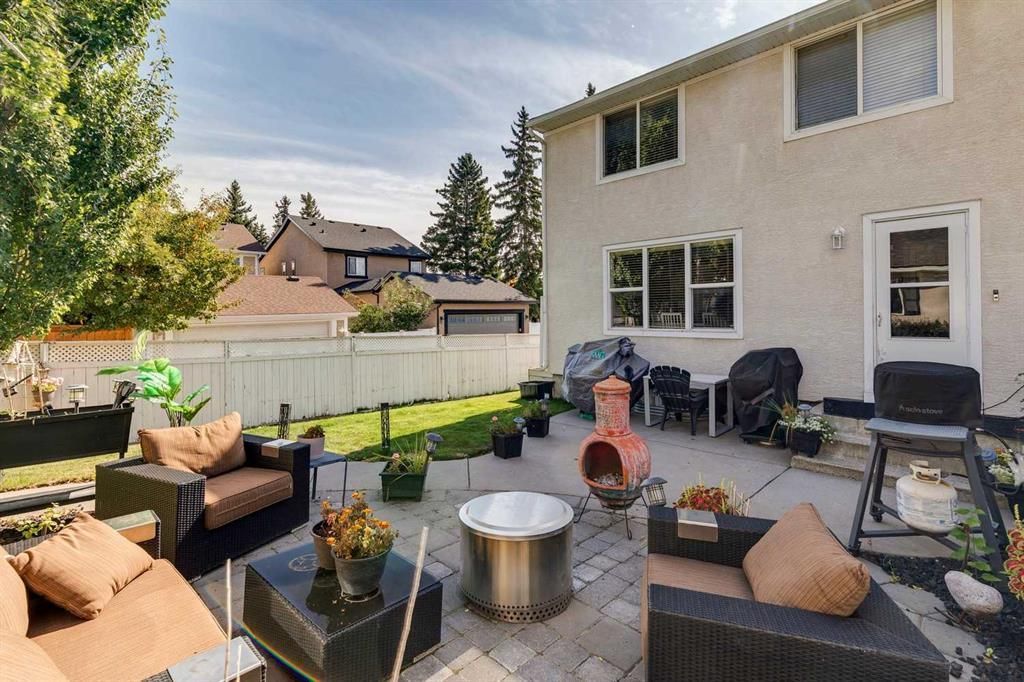 Patio seating area with wicker chairs, fire pit, and lawn beside a white two-story house