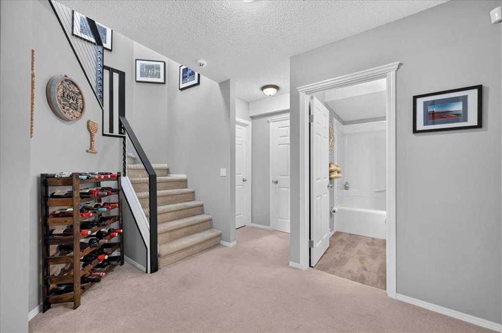 Beige-carpeted home hallway with stairs, open bathroom door, and wall decor.