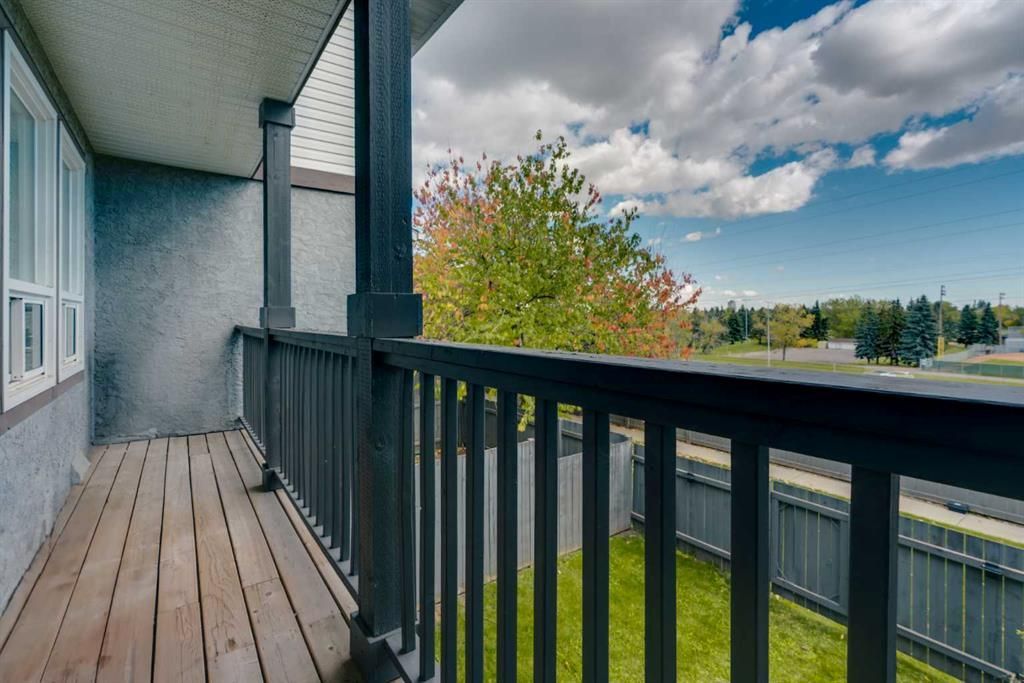 Wooden balcony walkway overlooking a green yard, trees, and cloudy sky beside a house exterior