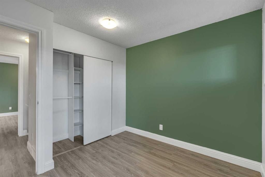 Empty bedroom with green accent wall, open closet, and wood-look flooring