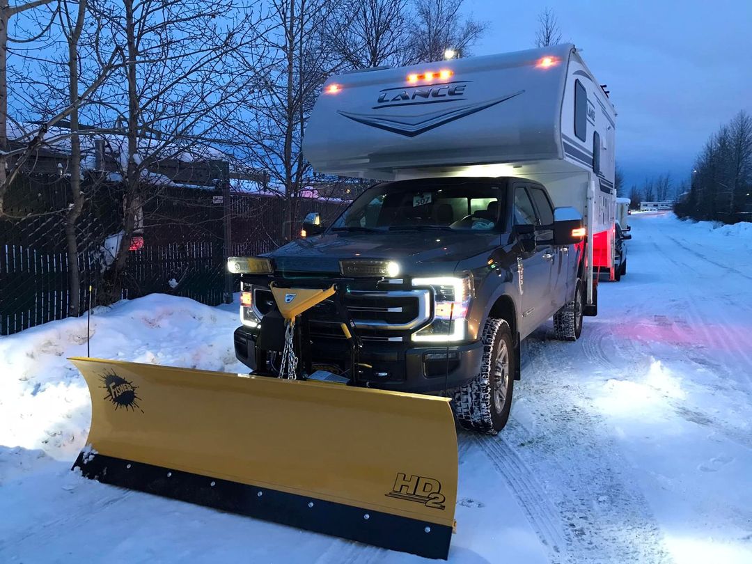 A truck with a snow plow attached to it is driving down a snowy road.