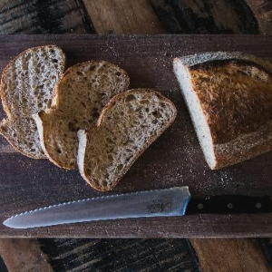 Sliced bread on a wooden cutting board with a serrated knife beneath it