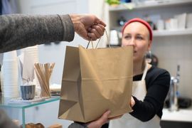 Handing a brown paper takeout bag across a counter in a café kitchen