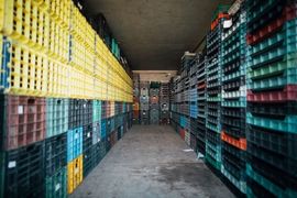 A narrow warehouse aisle lined with stacked plastic crates in yellow, blue, and teal.