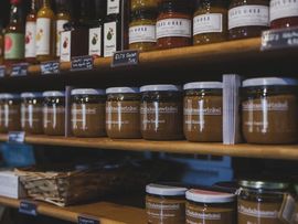 Shelves of glass jars filled with brown preserves in a deli or market display