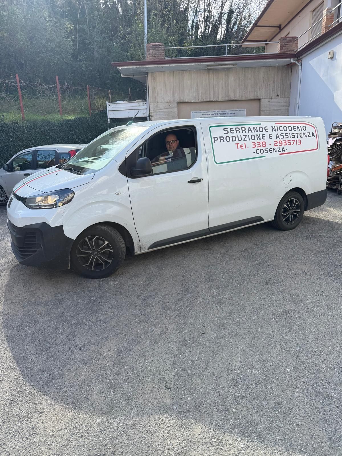 Furgone bianco con scritta sulla fiancata parcheggiato sulla ghiaia, con una persona al posto di guida.