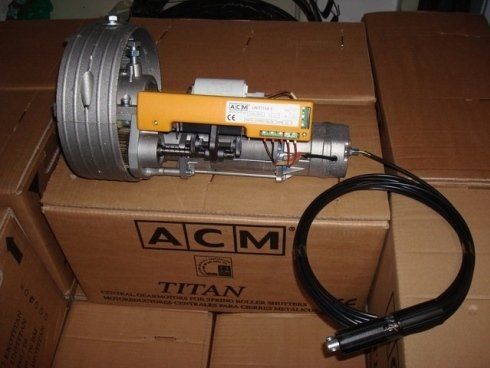 Motore per tapparelle ACM Titan, scatola di controllo gialla, cavo nero, appoggiato su una scatola di cartone.