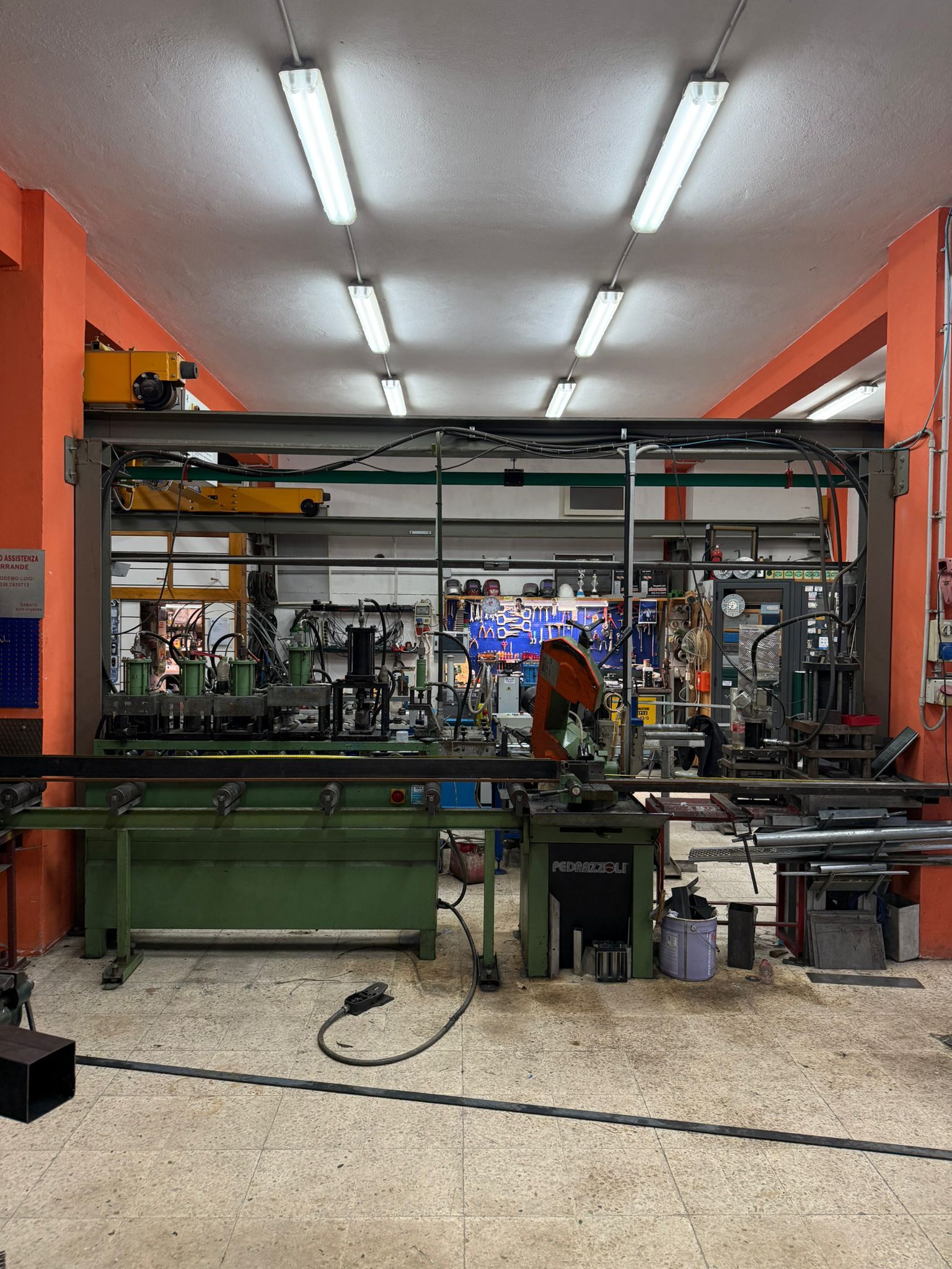 Interno dell'officina con macchinari, illuminazione fluorescente e pareti arancioni.