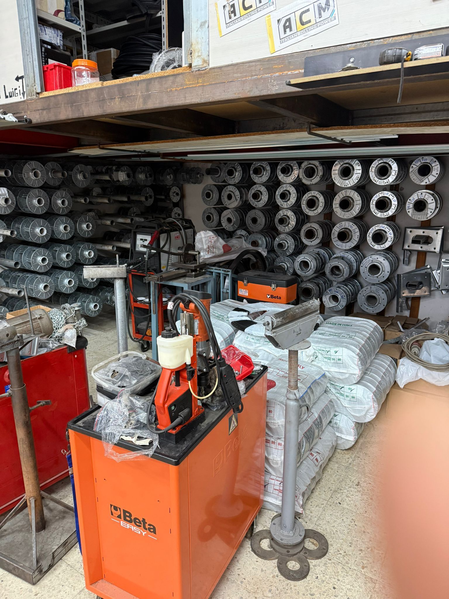 Interno dell'officina con macchinari, pezzi sugli scaffali e un armadietto arancione per gli attrezzi.