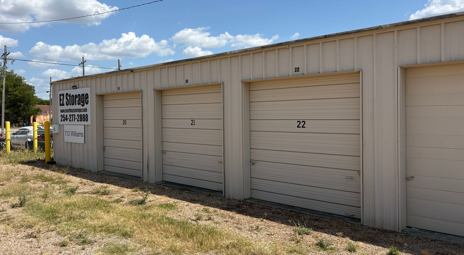 Row of beige Marlin EZ Storage unit doors on a small metal building under a sunny blue sky