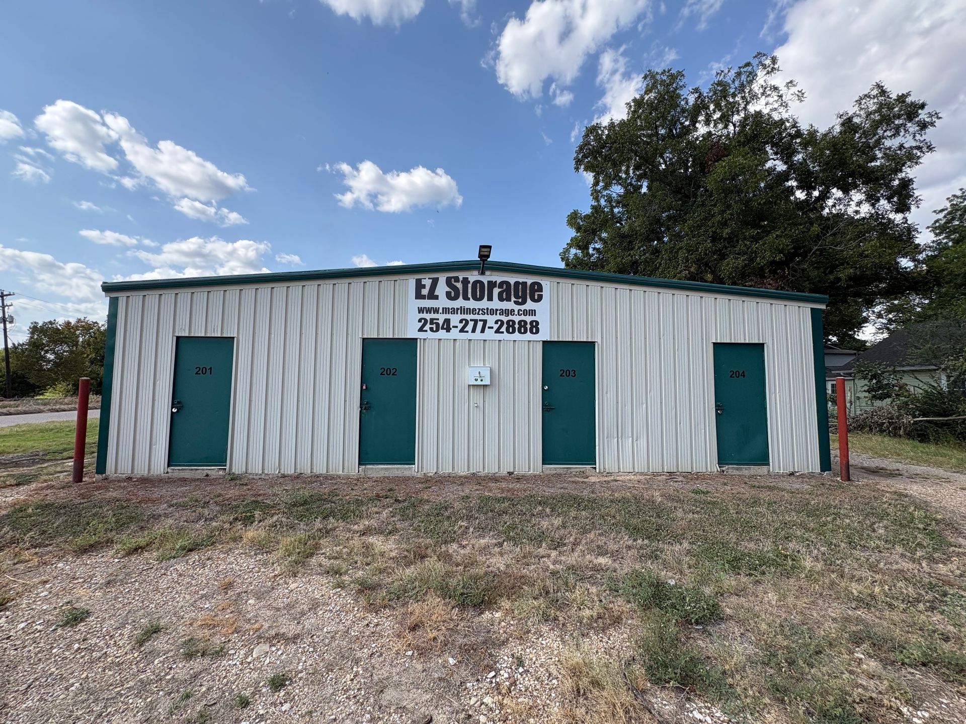Small white Marlin EZ Storage building with teal doors and sign under a cloudy blue sky