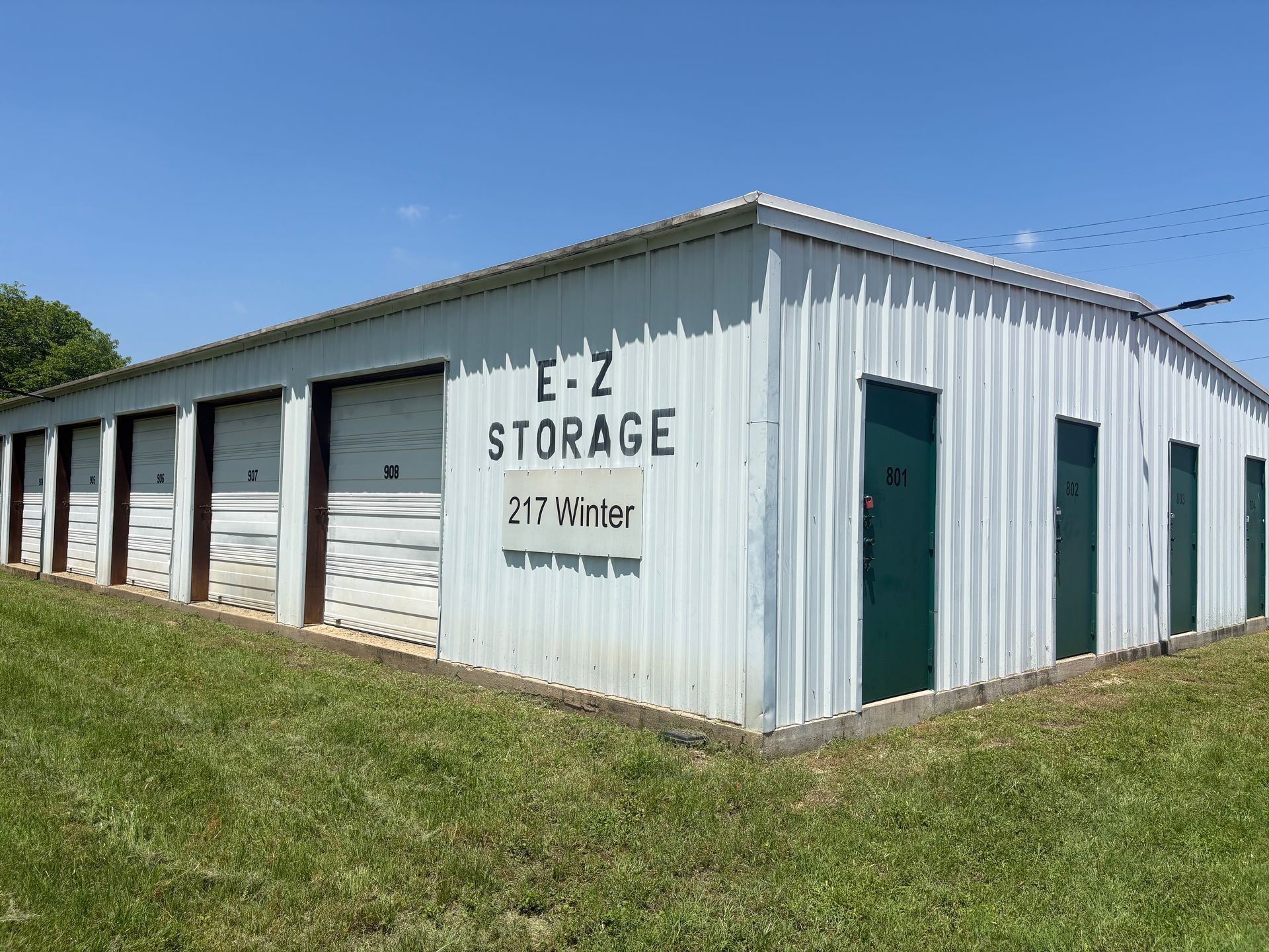 White metal EZ Storage building with garage doors on a grassy lot under a blue sky.