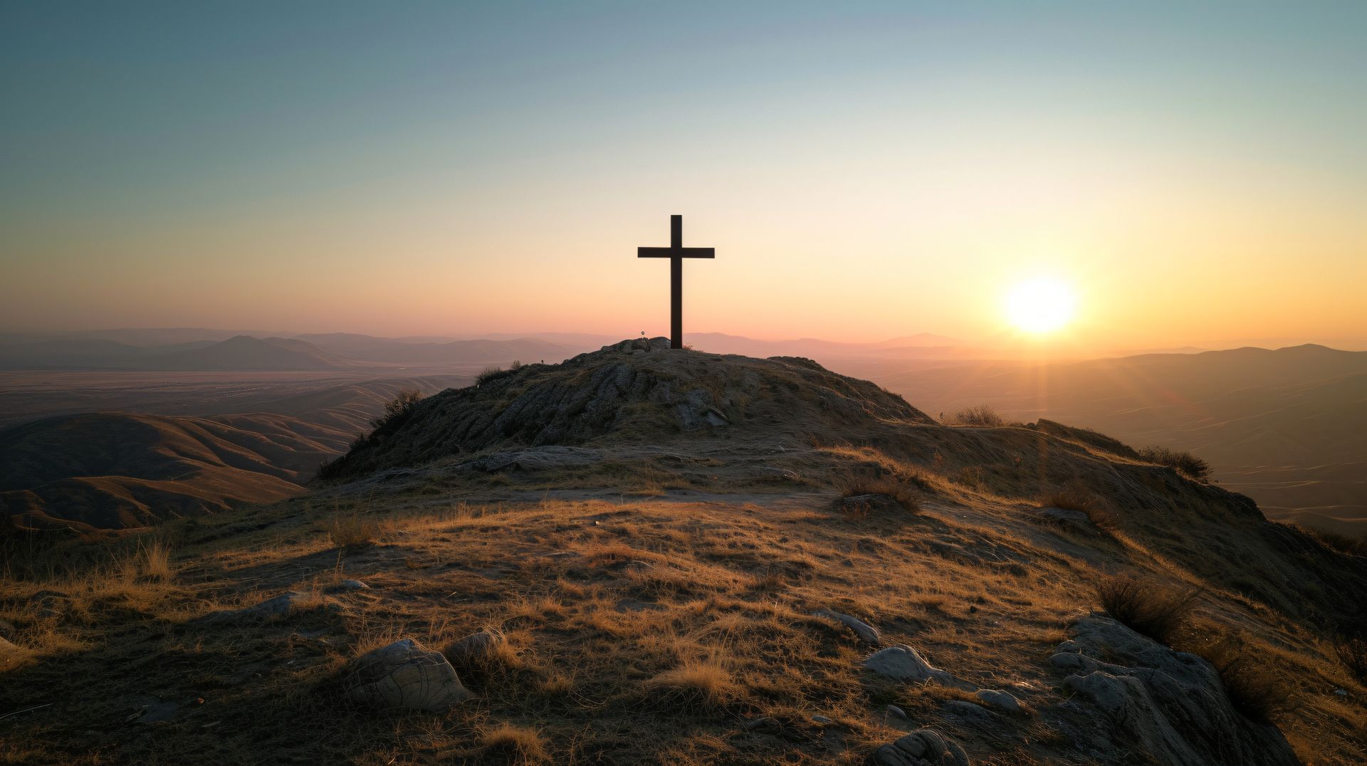 Cross on a rocky hill at sunrise with a warm glowing horizon