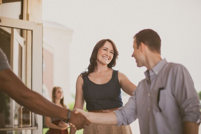 People shaking hands in a bright office, with a smiling woman in the background