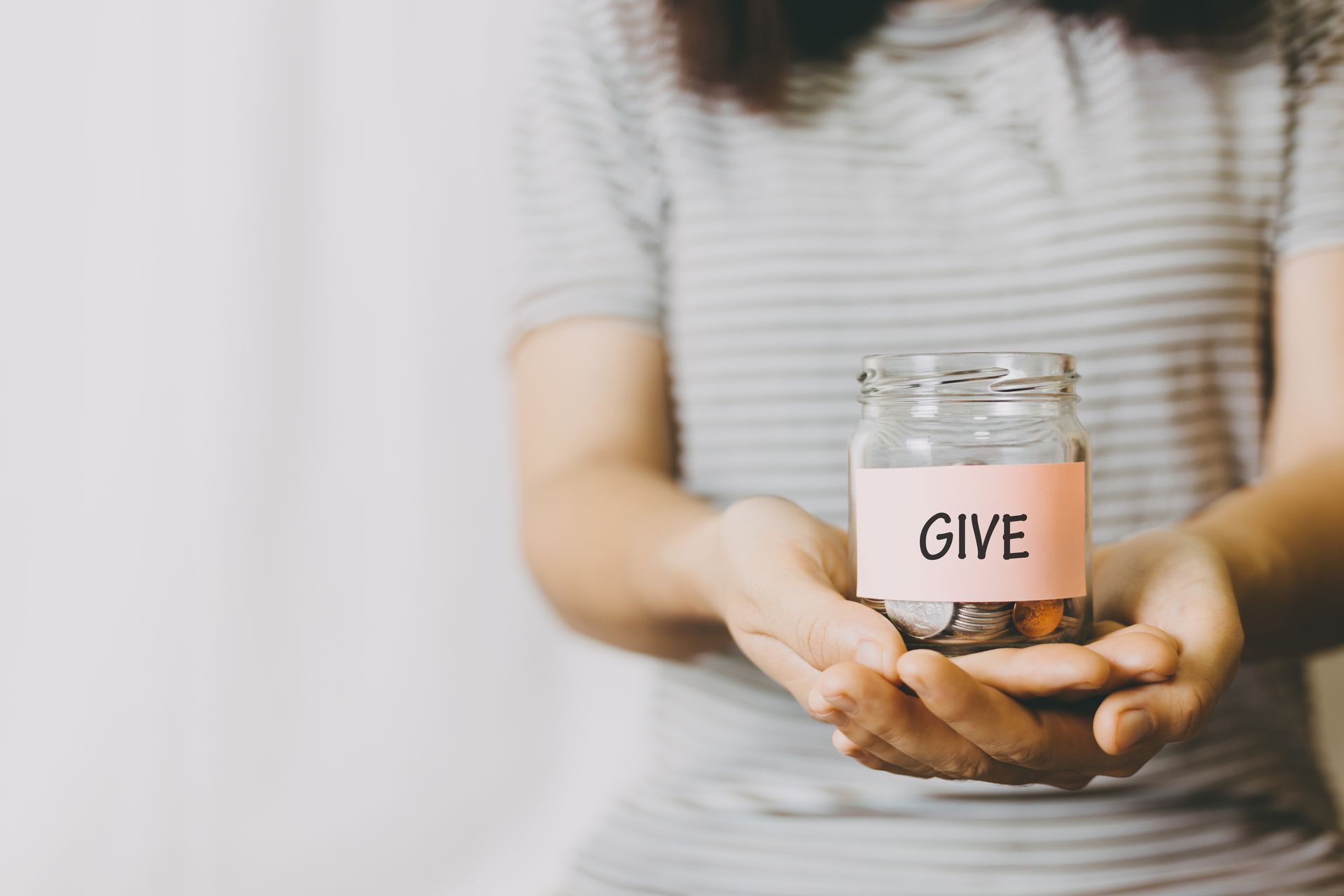 Hands holding a glass donation jar labeled “GIVE”