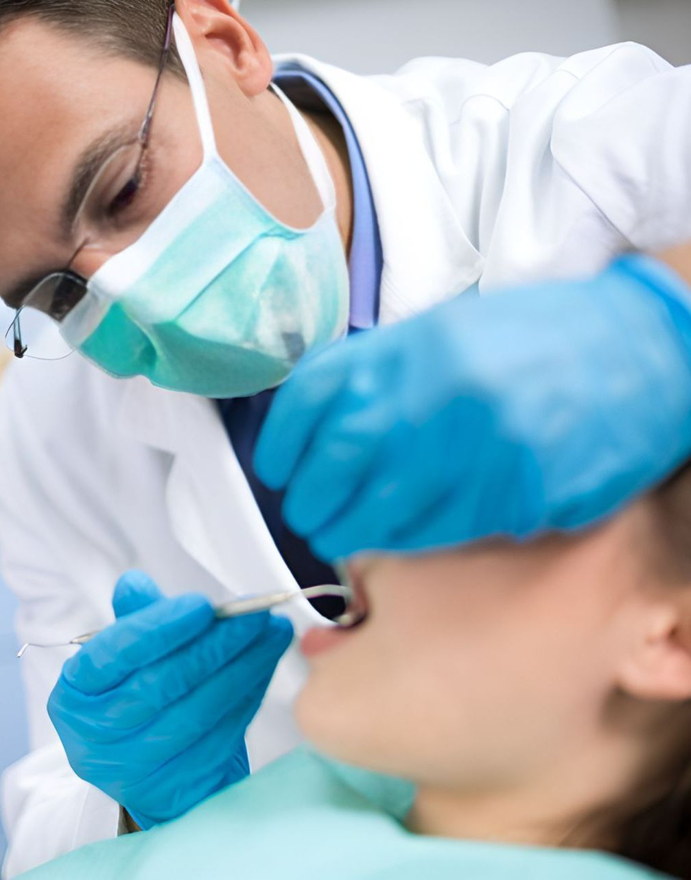 A Dentist Wearing a Mask and Blue Gloves Examines a Patient's Teeth — Graham Johnson Dental Surgery In Jesmond, NSW