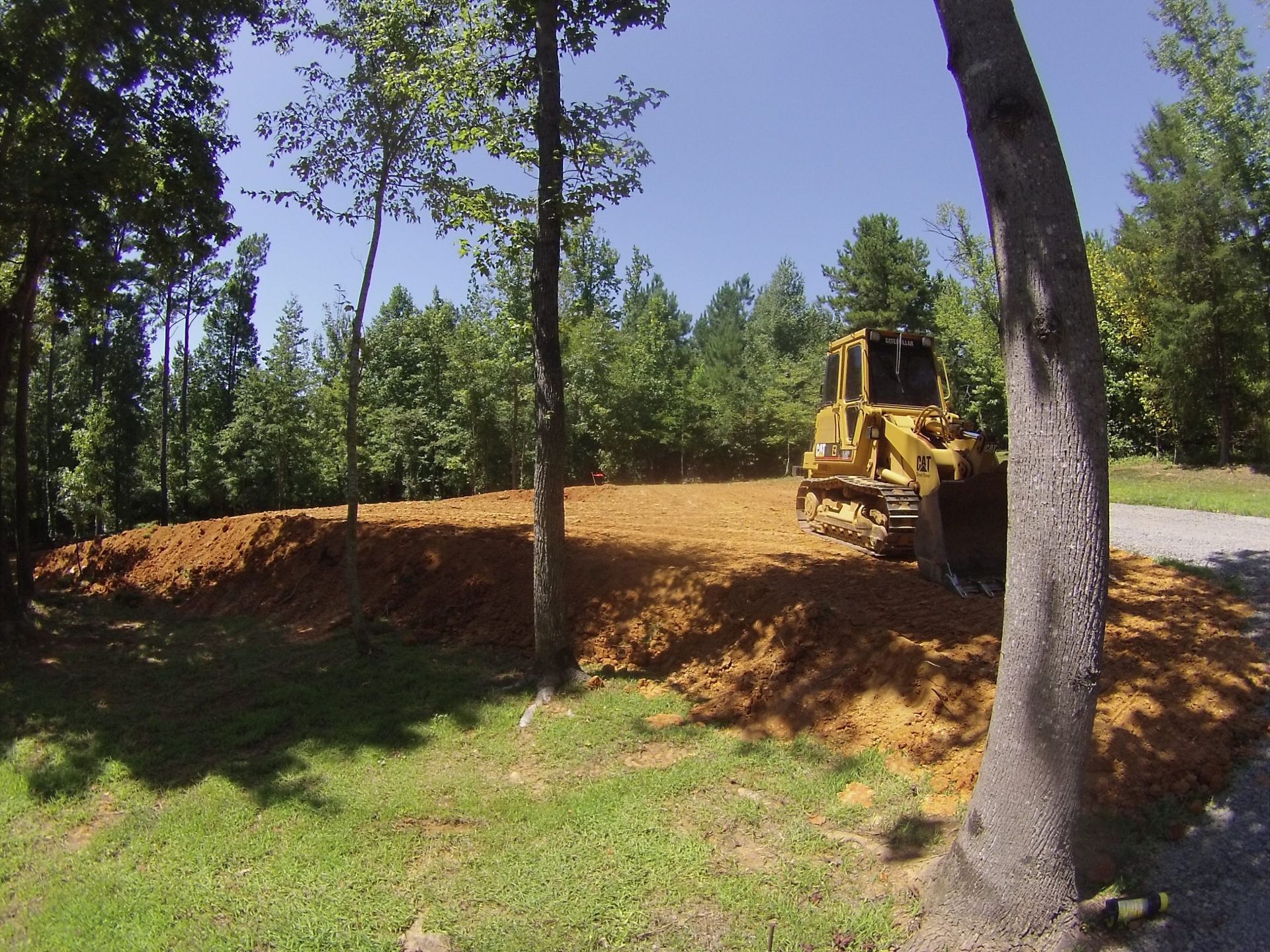 Yellow bulldozer clearing dirt in a wooded area beside a road