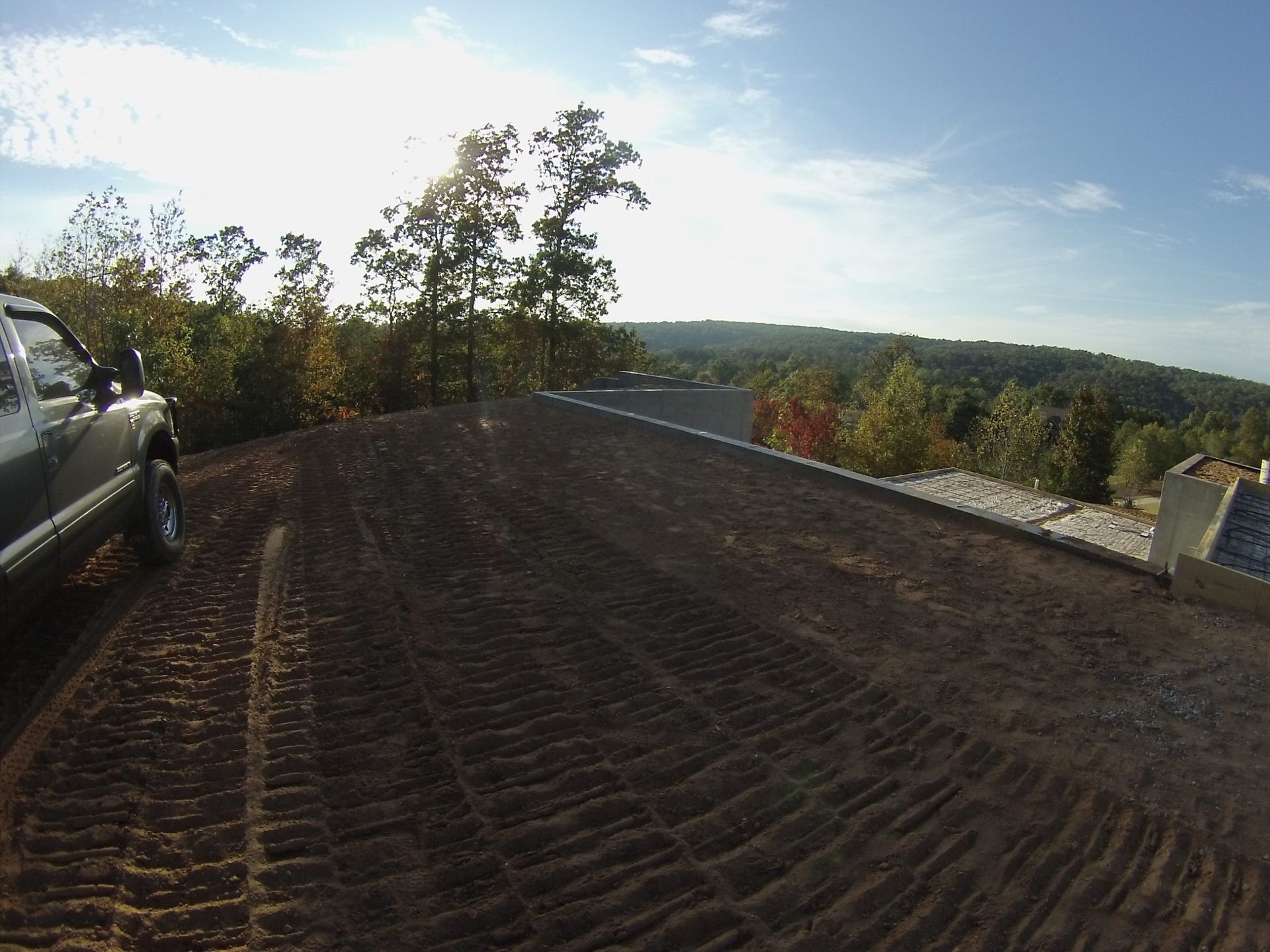 Gravel driveway overlooking a wooded valley at sunset, with a parked car on the left