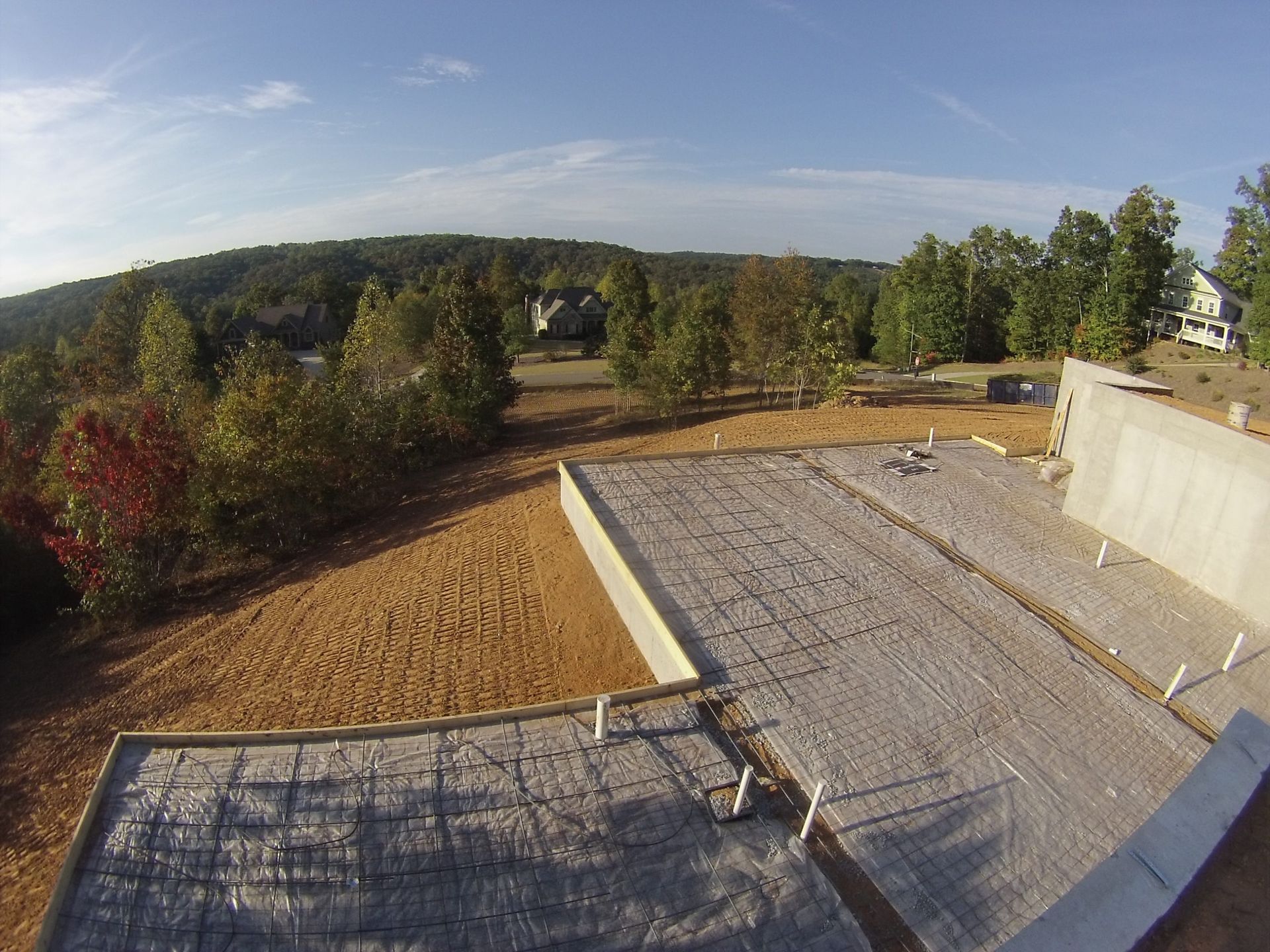Landscape view of a suburban lot with gravel, trees, and hills under a clear blue sky