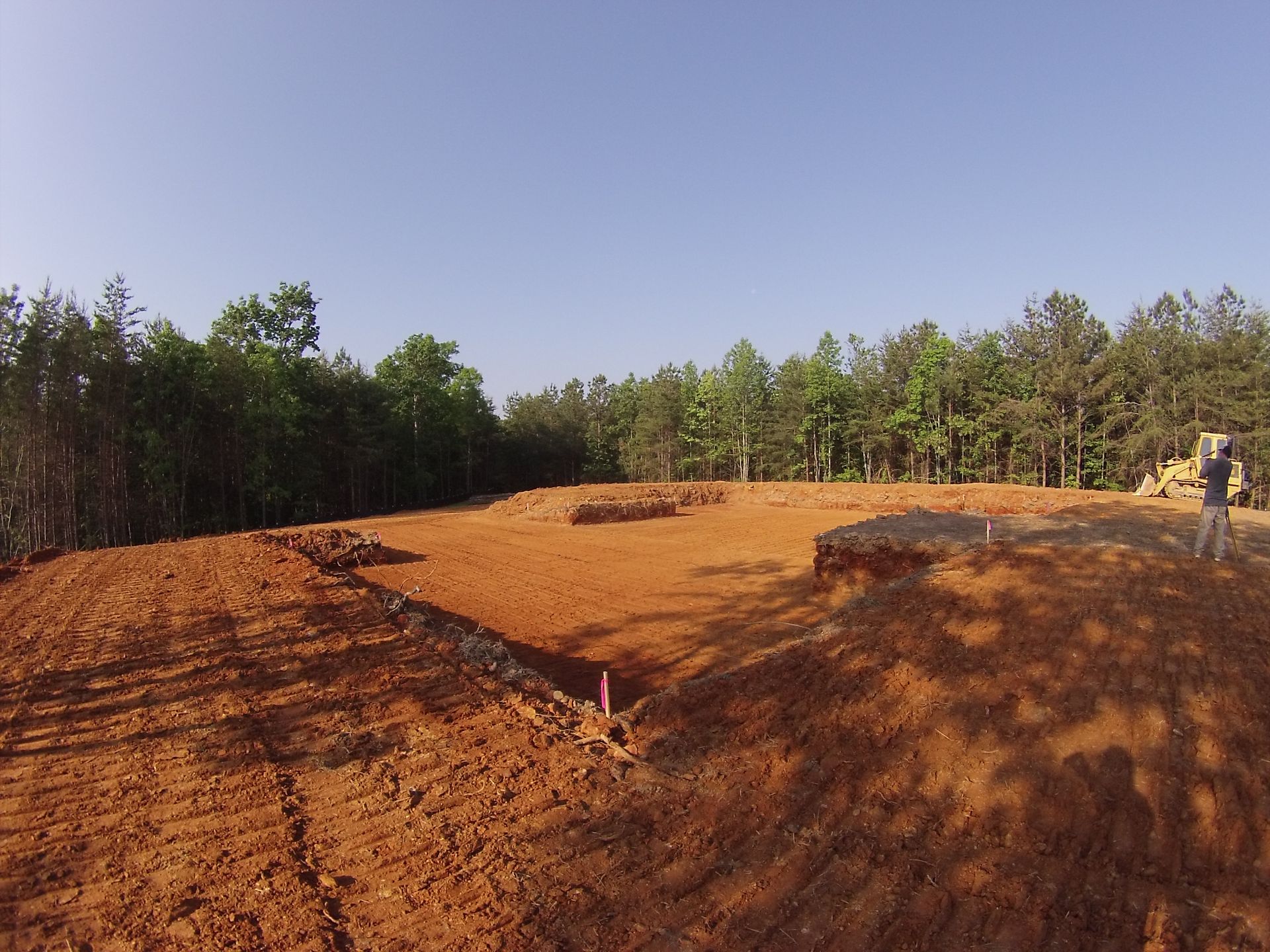 Dirt motocross track with berms and a person standing near the right edge, trees in the background