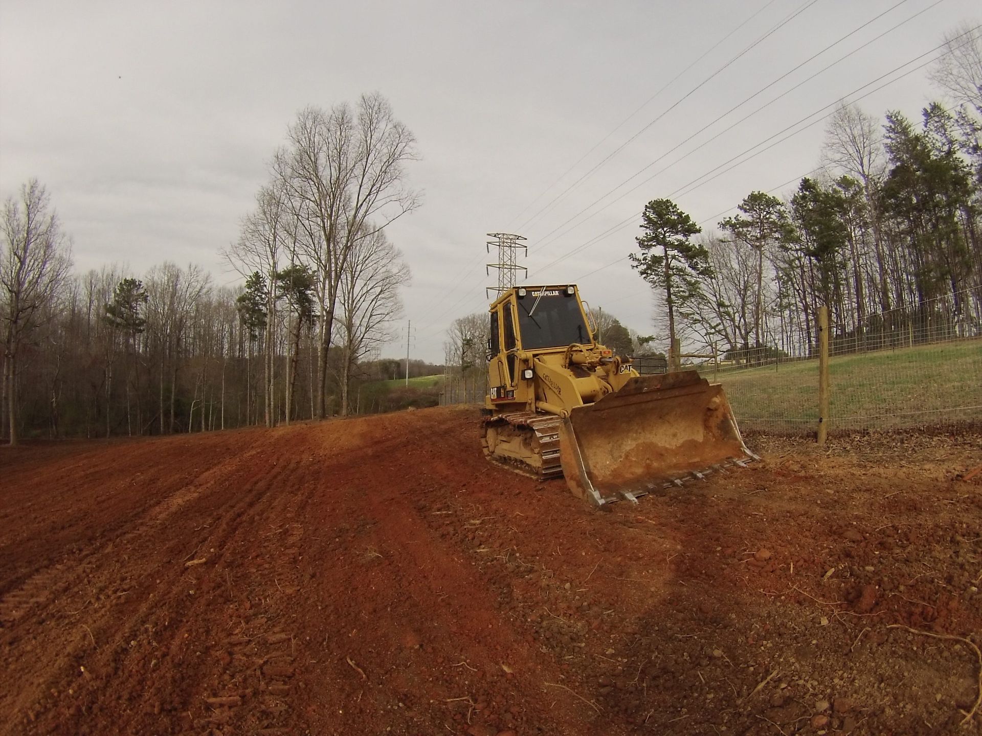 Yellow bulldozer grading a red dirt road on a cloudy construction site