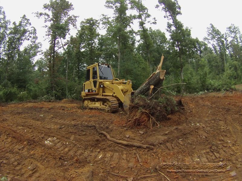 Yellow bulldozer clearing a muddy forest lot with uprooted trees and dirt piles