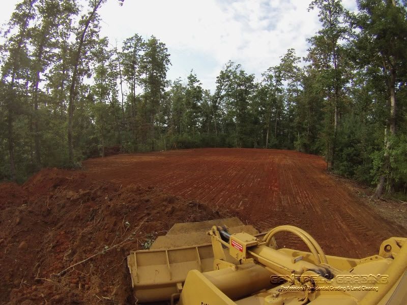 Yellow bulldozer clearing a red dirt road in a wooded area