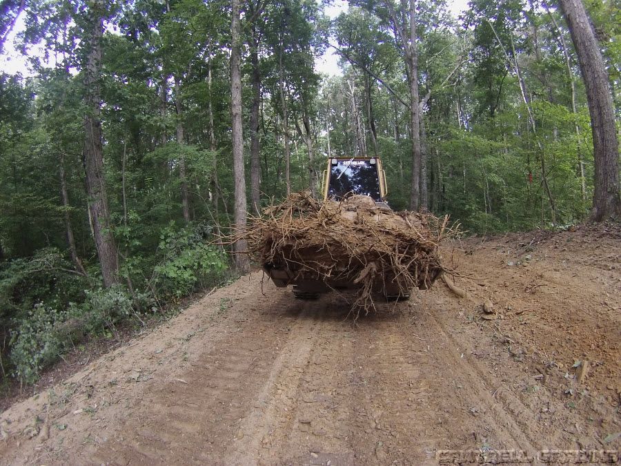 Bulldozer pushing a large pile of dirt down a muddy forest road