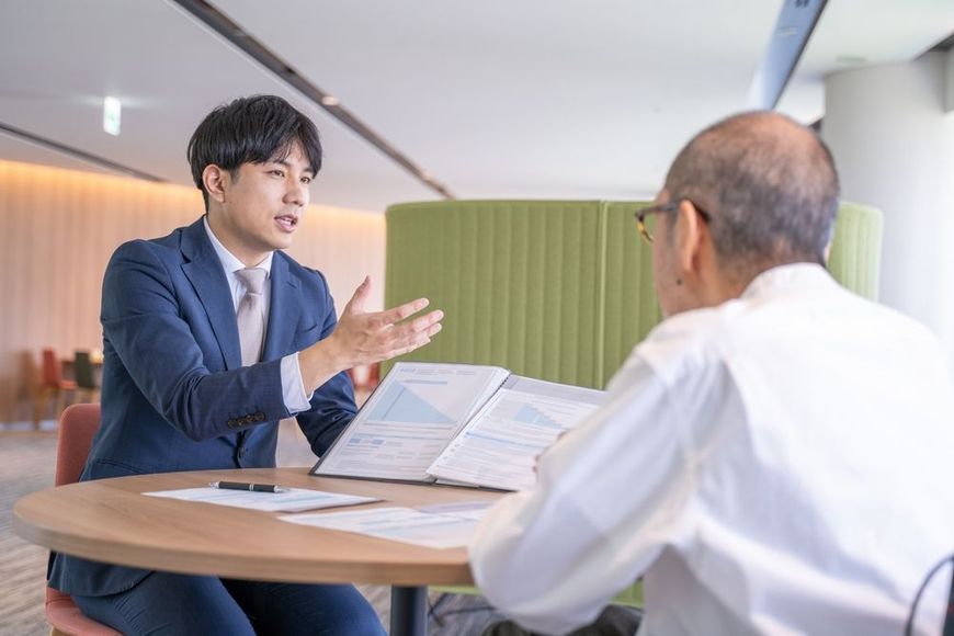 Two people discuss documents at a table in a bright office setting.