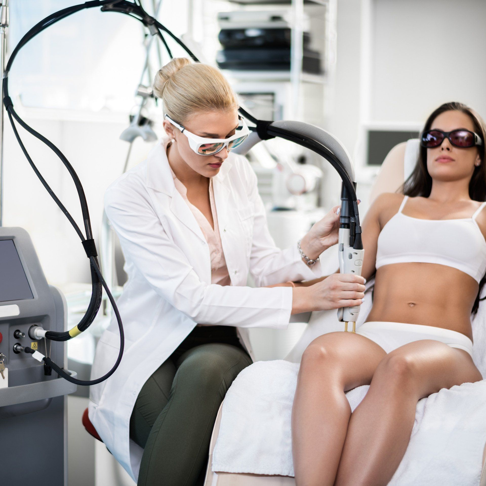Woman receiving laser hair removal treatment on her leg. Doctor adjusts the device, wearing eye protection.