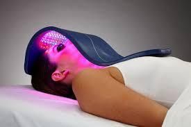 Woman receiving red and blue light therapy on her head and face while lying down.