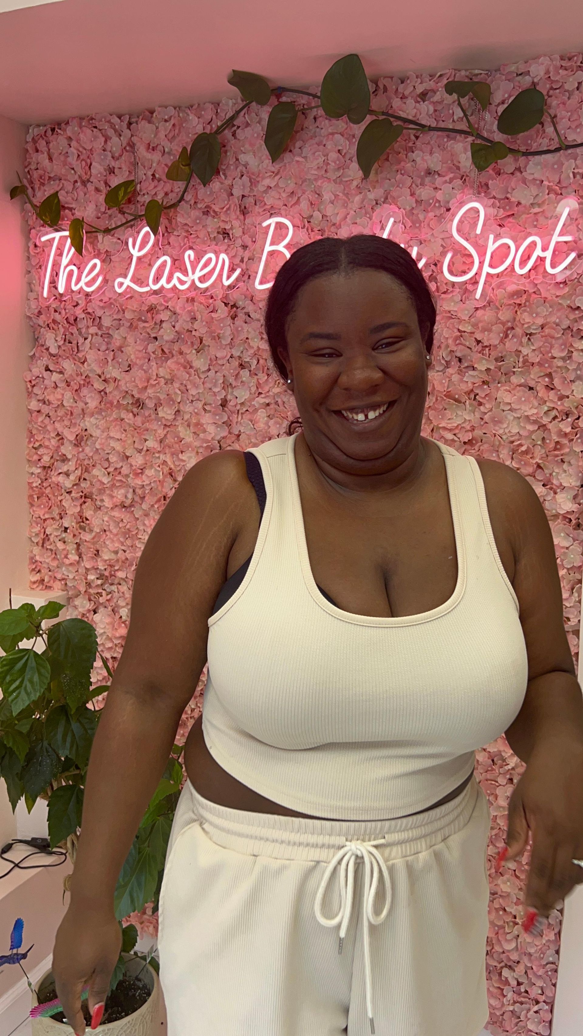 Woman smiling in a white outfit, in front of a pink flower wall. 