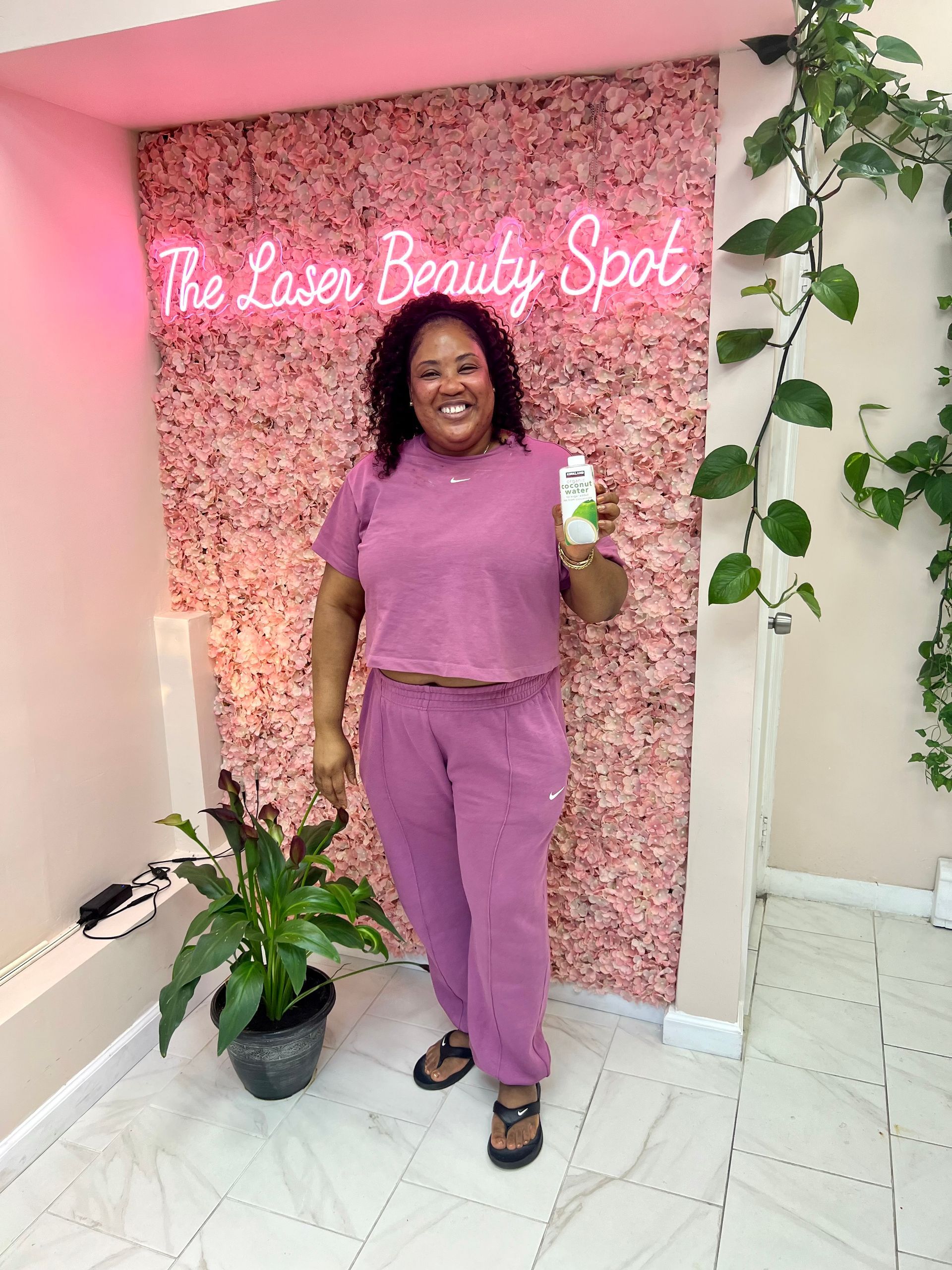 Woman in pink outfit holding a beverage, standing in front of a pink wall with 
