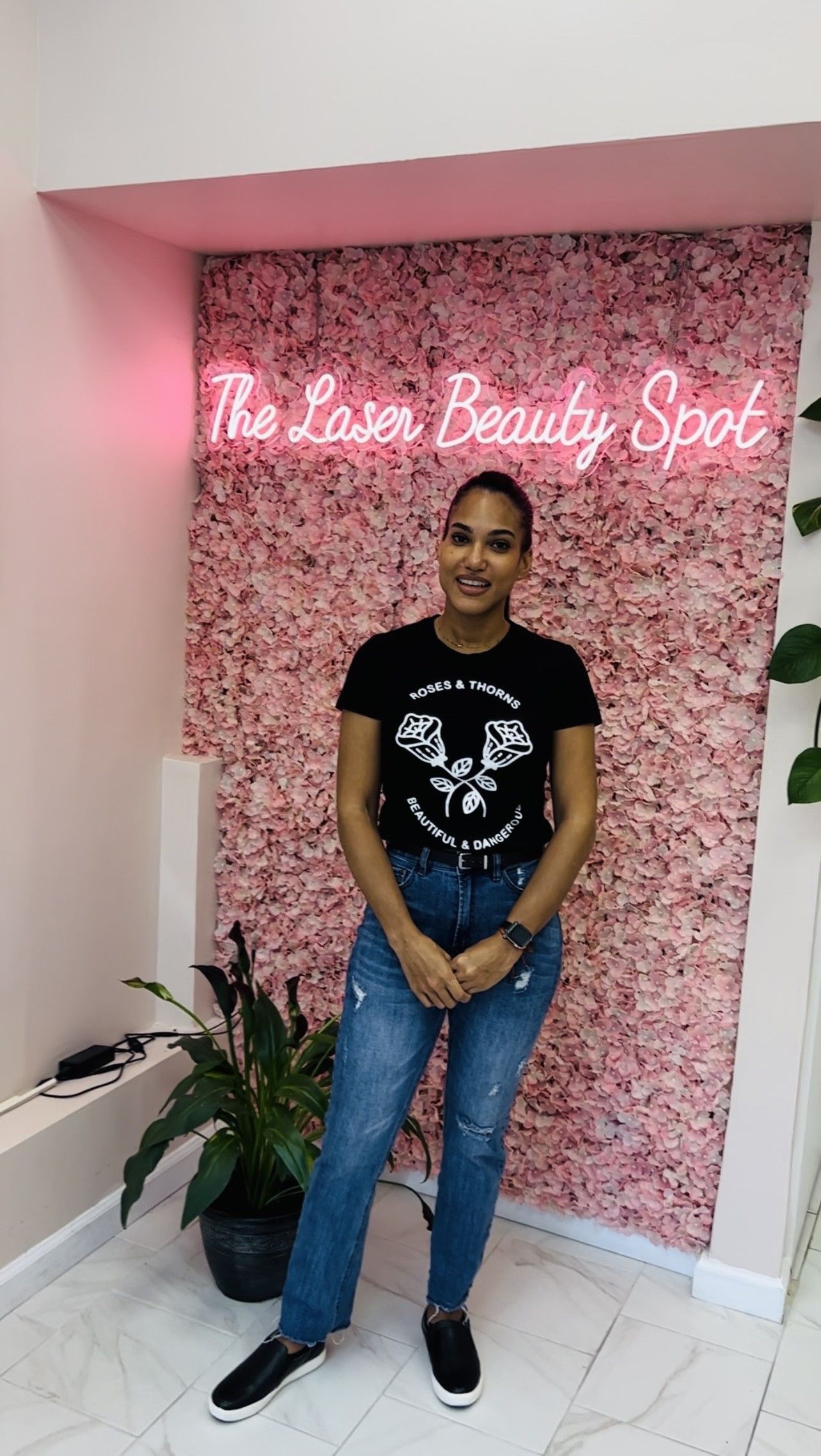 Woman standing in front of pink floral wall with neon sign 