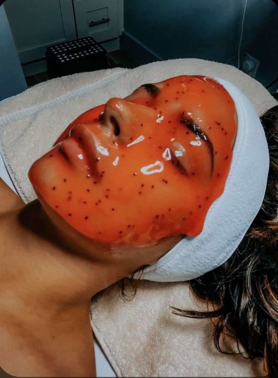 Person with facial mask, orange with dark specks, wearing a white spa headband, lying down.