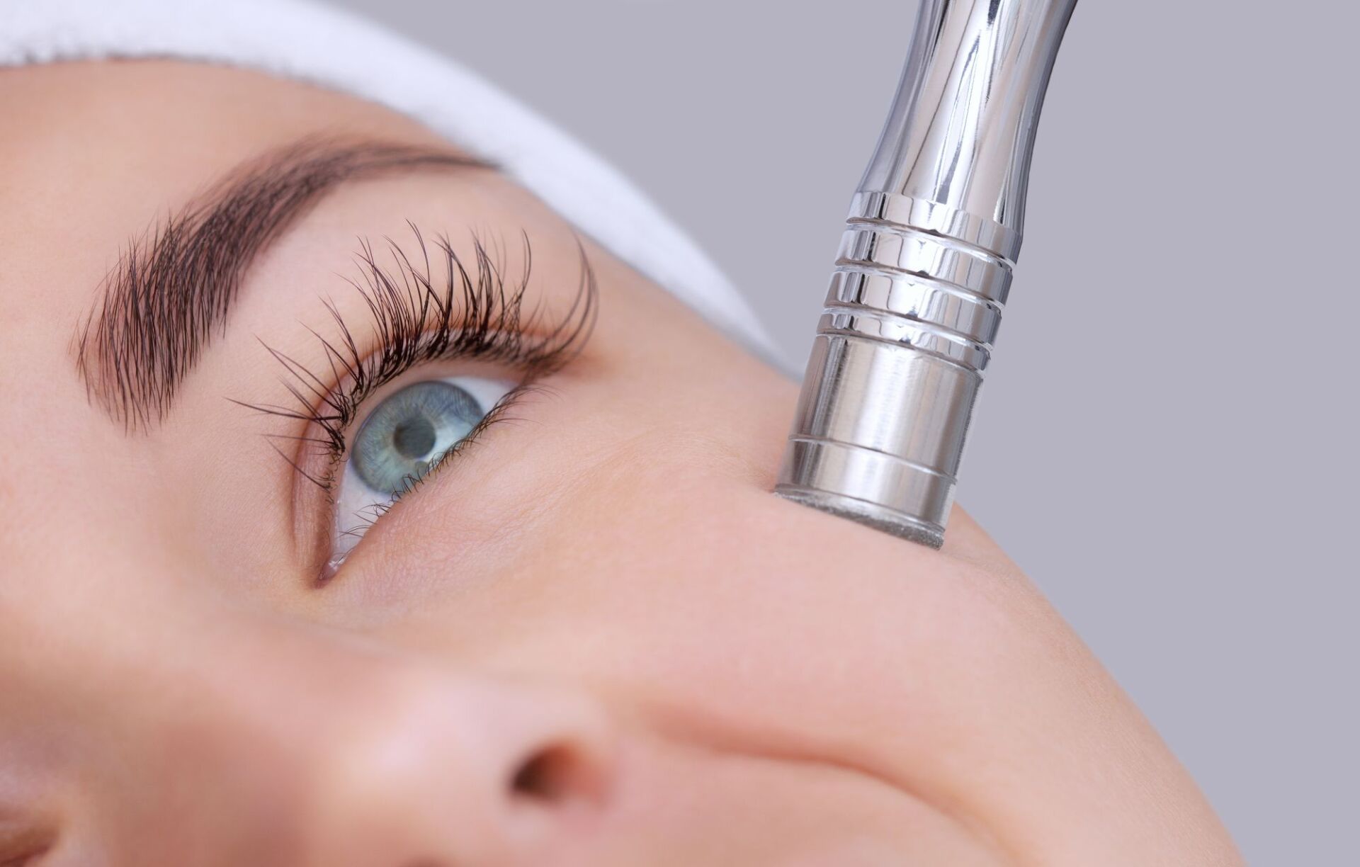 Woman receiving a microdermabrasion facial treatment, close-up with device touching skin near the eye.