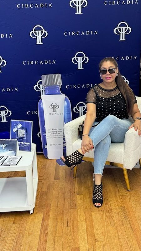Woman in sunglasses sits near Circadia product display. Background with logo, seated on a white chair.