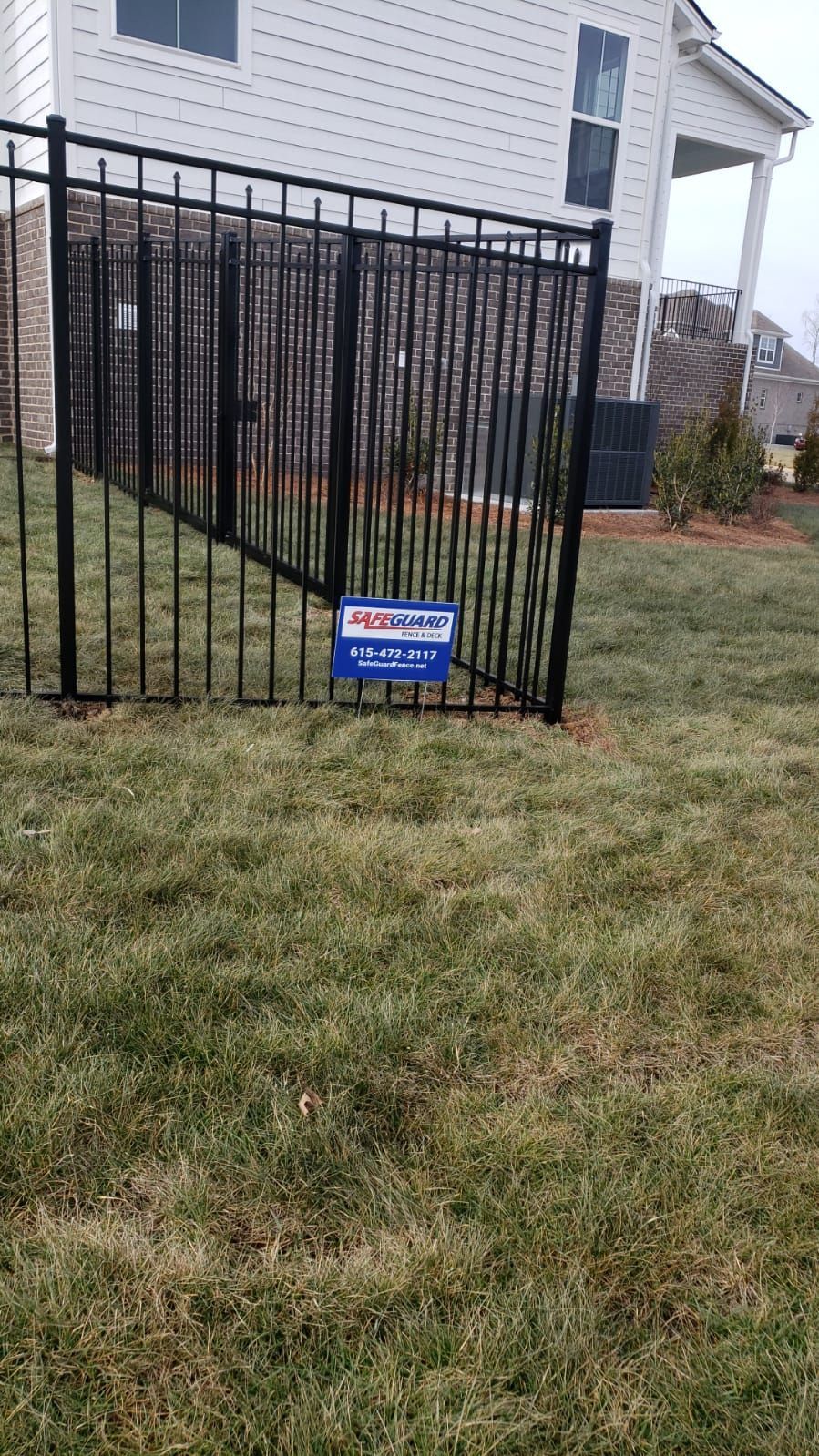 Black metal fence in a yard with a sign, house in background.