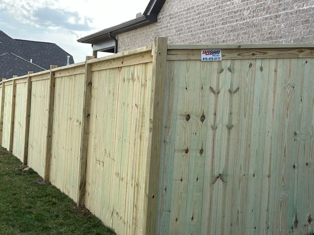 Wooden privacy fence along a brick building, with green grass in foreground.