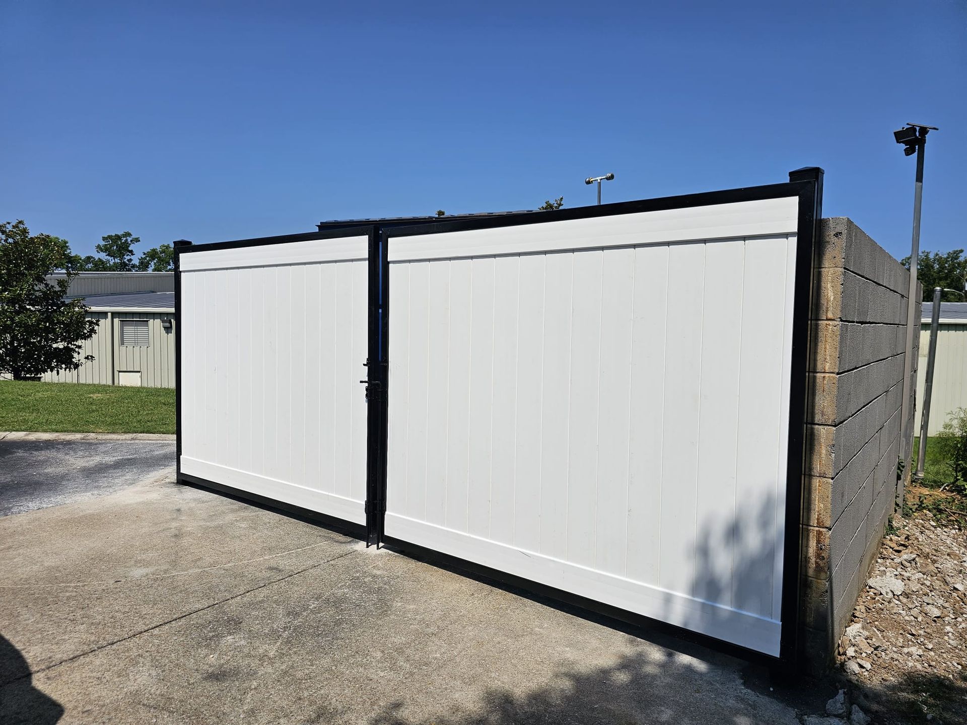 White vinyl gates with black frame, next to a concrete wall on a sunny day.