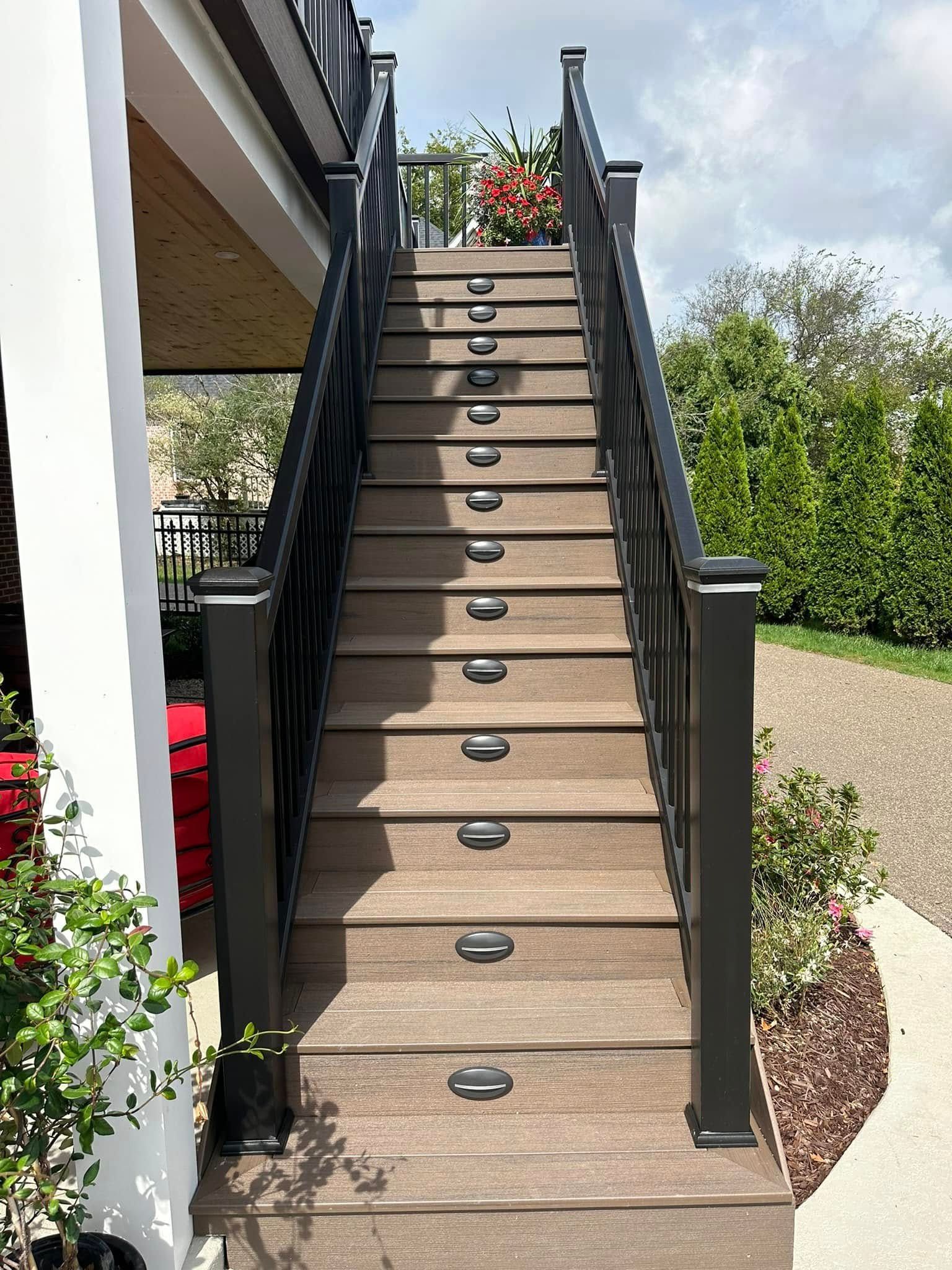 Wooden outdoor staircase with black railings and step lights, leading upwards.